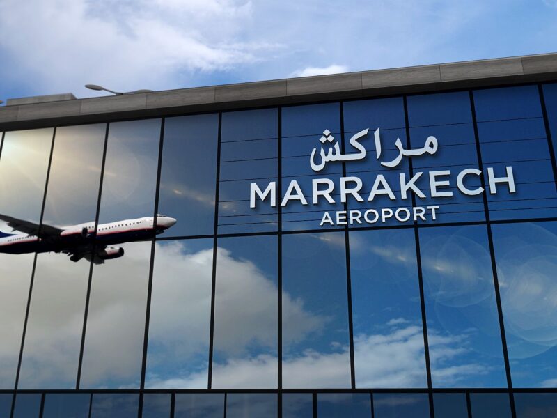 Exterior view of Marrakech Airport with an airplane flying above and reflective glass windows.